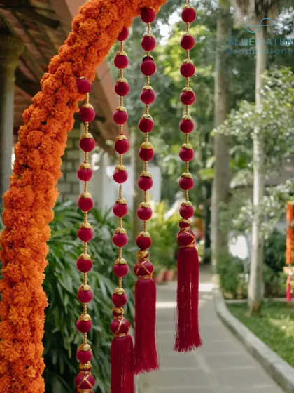 A close-up of a hanging decoration made of marigolds and red velvet tassels, showcasing the handcrafted details.