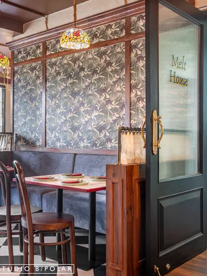 Booth seating at Melthouse is made intimate with wood paneling and patterned wallpaper. The reeded glass on the door adds a touch of privacy and vintage charm, contributing to the old-world pub aesthetic.