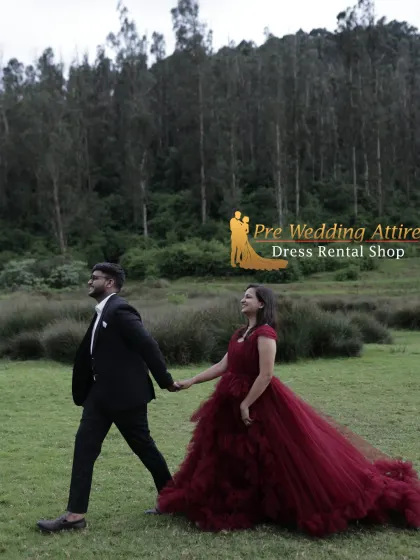 A couple walking hand-in-hand through a field. The woman wears a ruffled maroon gown, and the man is in a classic black suit, creating a beautiful contrast with the natural landscape.