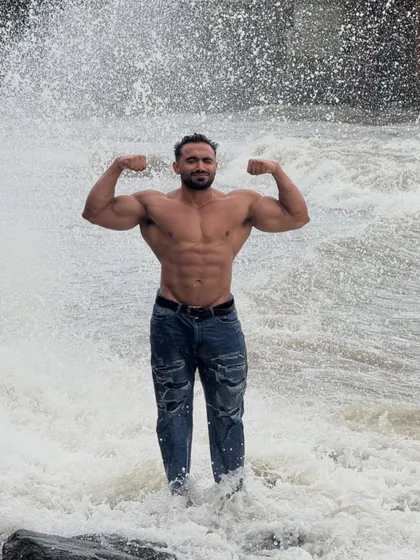 Dilwale. A powerful double biceps pose in front of a splashing wave.