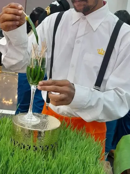 A chef carefully places pickled green chilies in a wine glass, part of a unique salad bar presentation.