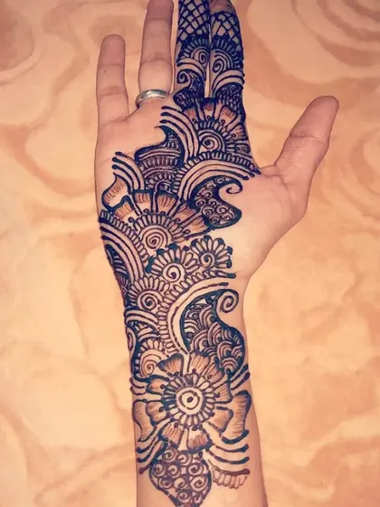 A bold and modern Arabic design on the palm. This style uses thick lines and intricate shading to create a dramatic and eye-catching floral pattern.