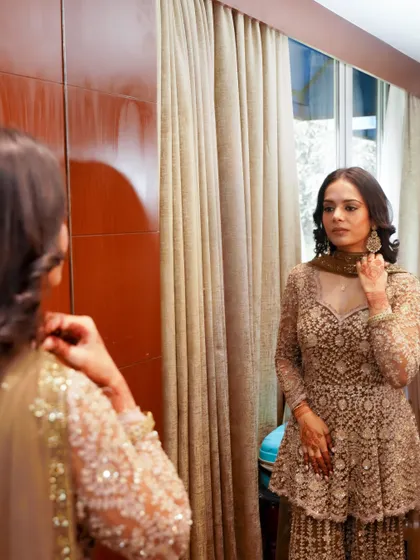 A full-length view of this soft glam look. The makeup is natural and radiant, perfectly complementing her elegant beige outfit for a wedding guest appearance.
