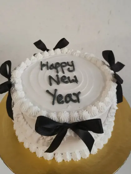 An elegant black and white themed cake for a stylish New Year's Eve party. The cake is decorated with delicate piping and black satin ribbons.