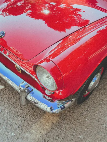 The beautiful red finish and classic headlight of a vintage car, with the trees of Mumbai reflected on its polished hood.
