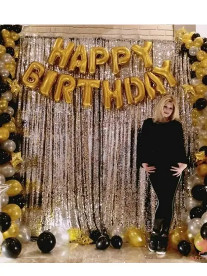 A glamorous birthday photo booth with a silver shimmer curtain and black and gold balloons. This is a great setup for adults' birthday parties.