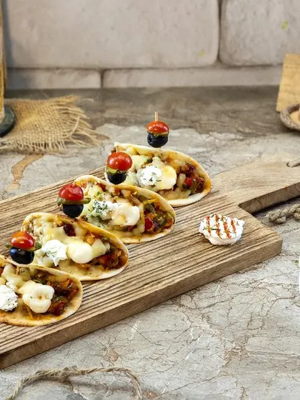 These mini naan pizzas were shot to look like the perfect shareable appetizer. The composition on the wooden board with fresh ingredients scattered around gives a relaxed, social vibe, ideal for a cafe or bar menu.