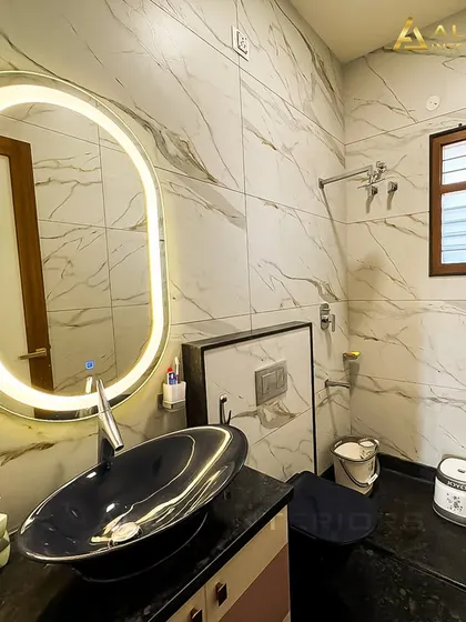 A modern bathroom with a large, oval backlit mirror and a stylish dark blue vessel sink. The white marble-patterned wall tiles keep the space feeling bright and clean.