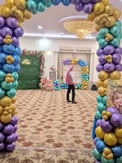 I create a complete experience, starting from the entrance. This balloon arch in teal, purple, and gold welcomes guests into the Krishna-themed baby shower celebration.