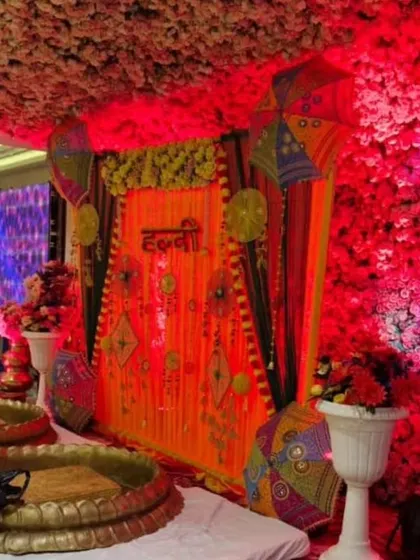 A grand indoor Haldi setup with a heavily decorated backdrop and a floral ceiling. The use of red lighting and traditional props creates a rich and opulent atmosphere.