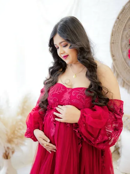 A close-up portrait capturing a moment of quiet reflection. The mom-to-be looks down at her bump with a gentle smile, dressed in a beautiful red gown.