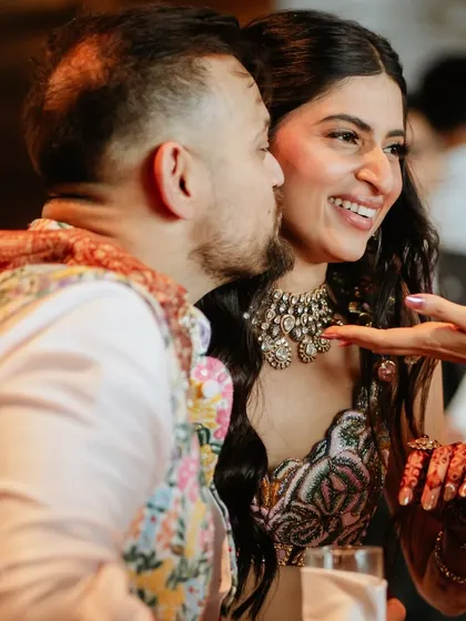 A candid interaction during the Sangeet. The bride's smile and glowing makeup light up the frame.