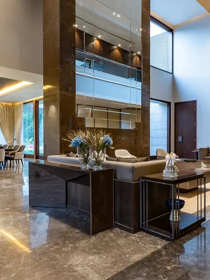 Designing for large, double-height spaces requires a careful balance of elements. In this farmhouse, we used minimalist furniture groupings to define different zones within the open-plan living area. A central pillar clad in mirrors and stone adds a dramatic touch while reflecting light and the surrounding space.