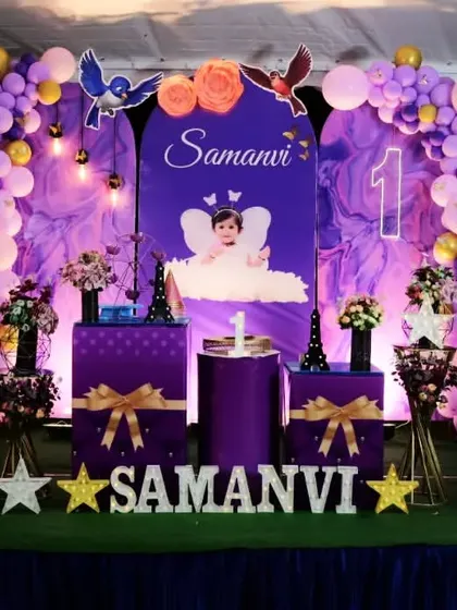 A royal purple princess theme for Samanvi's first birthday. The decor features cutouts of Sofia the First, a personalized milestone board, and elegant gift box props.