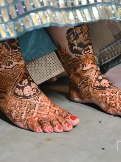 A close-up of a bride's feet, adorned with intricate mehandi. The design features elephants and floral motifs.