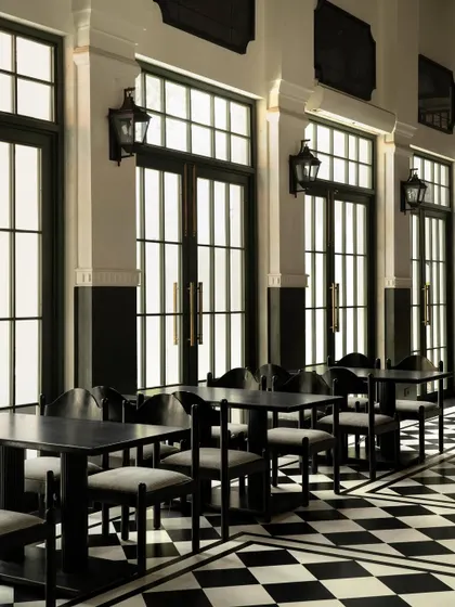 The gallery at Elgin Cafe, where a rhythmic series of tall, dark-framed doors creates a strong linear perspective. The monochrome checkerboard floor and classic lantern-style sconces reinforce the contemporary-classic aesthetic.