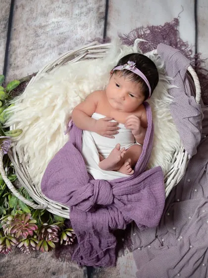 Another look at this lovely purple setup. The baby is wrapped in a lavender bow and placed in a white basket, surrounded by purple flowers and greenery.
