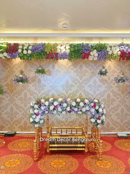 A full stage view for a cradle ceremony. The floral arch frames the space beautifully, with hanging birdcages adding a whimsical touch to the elegant wallpapered backdrop.