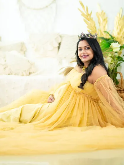 A beautiful portrait of a mom-to-be relaxing in a yellow gown on the floor of our studio. The wide shot captures the flowing fabric and the serene setting.