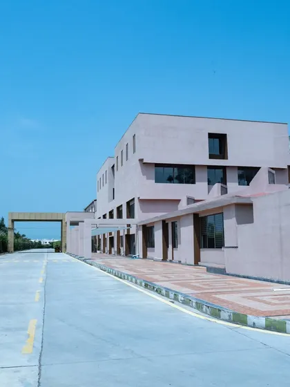 A long-range view of the Konark Academy campus, showing the main road leading to the entrance. The building's soft beige facade stands out against the clear blue sky, presenting a clean and inviting image.