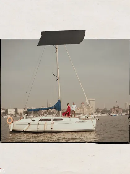 A wide shot showing the scale of the yacht against the backdrop of the Mumbai harbor and the Taj Mahal Palace Hotel.