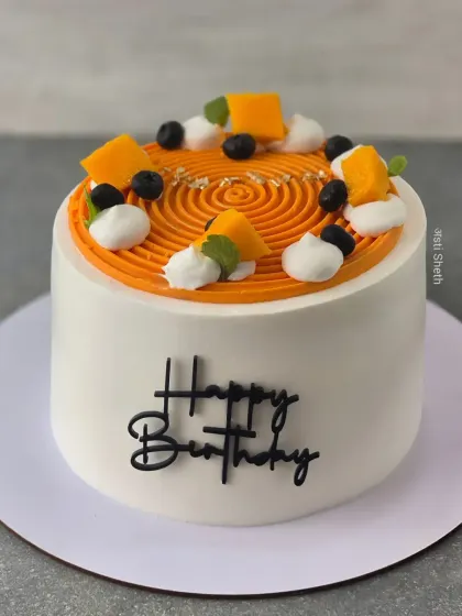 A beautiful Alphonso mango cake with a spiral piping design on top. It's decorated with fresh mango chunks and blueberries for a simple, elegant look.
