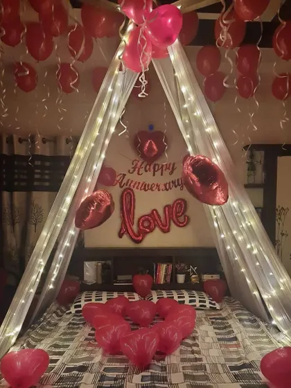 I can transform your bedroom into a romantic retreat for an anniversary. This bed canopy setup includes fairy lights, red heart-shaped balloons, and "LOVE" foil balloons for a classic and heartfelt surprise.
