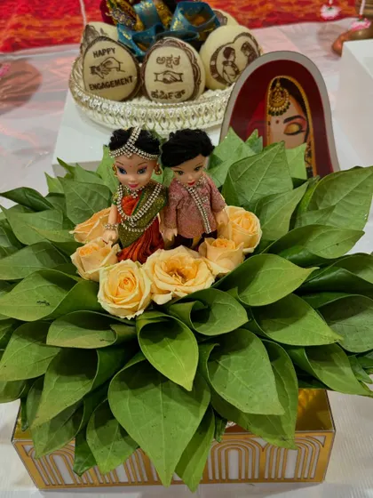 An eco-friendly engagement platter made with fresh betel leaves and roses. The couple dolls and personalized coconuts in the background add a special touch to the arrangement.