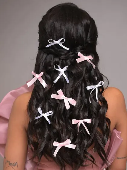 A whimsical and romantic open hairstyle featuring soft waves decorated with multiple small pink and white bows. This look is perfect for a playful and feminine fashion shoot.