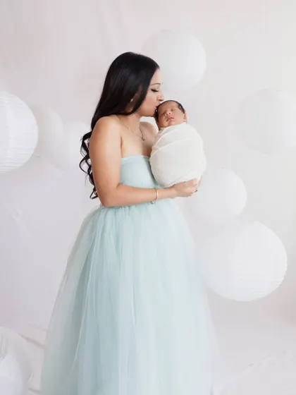 A mother's first portrait with her newborn. Dressed in a beautiful tulle gown, she holds her baby close in a dreamy, all-white setting.