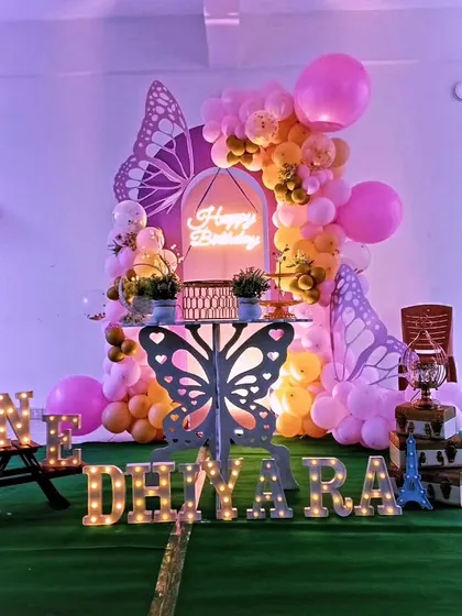 This coustamised butterfly theme for Dhiyara's first birthday features a unique arched backdrop, a neon "Happy Birthday" sign, and a butterfly-shaped table, creating a modern and stylish look.