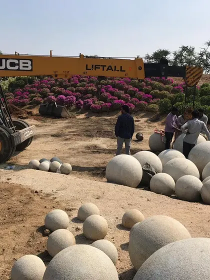 The installation process for the stone spheres at our Hyderabad site. This behind-the-scenes look shows the scale of the project, with a JCB crane and a large team at work.