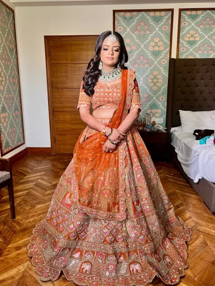 A full-length view of the bride's stunning orange lehenga, showing how the makeup complements the vibrant color.