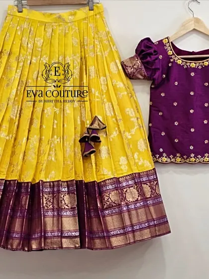 A vibrant yellow Banarasi silk lehenga paired with a contrasting purple blouse. The blouse has delicate butti work, and the skirt features a wide, intricately woven purple and gold border.