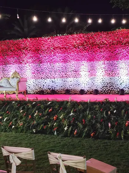 A massive floral wall created with bands of red, pink, and white flowers provides a stunning backdrop for this event. The elegant chaise lounge adds a classic touch to the vibrant and modern stage design.