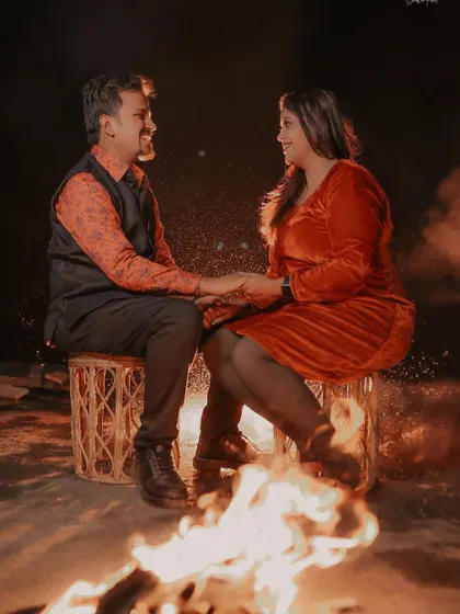 A cozy and romantic pre-wedding shot of a couple by a bonfire at night, creating a warm and intimate atmosphere.