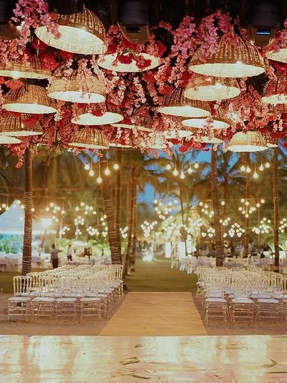 Beach weddings are a whole VIBE. ❤️ For this evening ceremony, we created a canopy of woven basket lamps and pink blossoms, casting a warm, romantic glow over the aisle as dusk settled in.