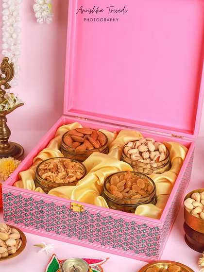 A vibrant pink Diwali dry fruit hamper, styled with traditional brass diyas and marigold flowers for an authentic festive feel.