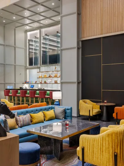 The main lounge area at Holiday Inn, Lucknow, is designed for comfort and social engagement. A mix of vibrant blue, yellow, and orange seating is arranged to create multiple conversation zones, unified by a large, colorful area rug.