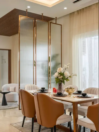 This dining space is defined by a beautiful fluted glass partition with a brass frame, which separates it from the living area without closing it off completely. The tan leather chairs and marble-topped table create a warm and sophisticated setting for meals.