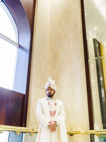 A more dramatic, low angle shot of Aakash. The high ceilings and grand architecture of the venue add a sense of scale and majesty to this groom portrait.
