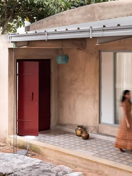 The passageway and main door of the 'Free Spirited by the Hills' farmhouse, as seen from the courtyard. The rustic stone wall, earthy tones, and bold red door create a beautiful composition that feels organic and deeply connected to the landscape.