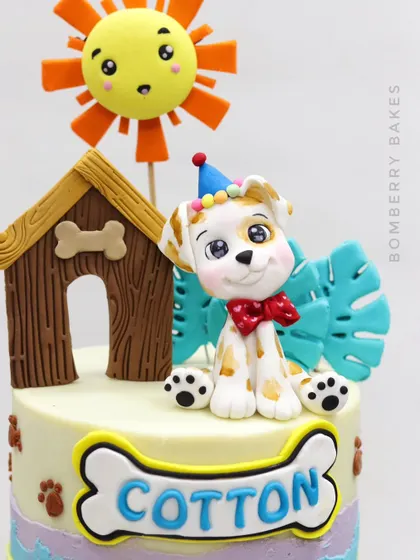 A fun, pet-themed cake celebrating a girl and her dog's birthday together. This piece features multiple fondant elements, including a cute puppy in a party hat, a doghouse, and a smiling sun.