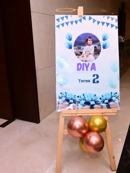 A welcome sign for a second birthday party, featuring the birthday girl's photo. The sign is placed on an easel and decorated with balloons to match the party theme.