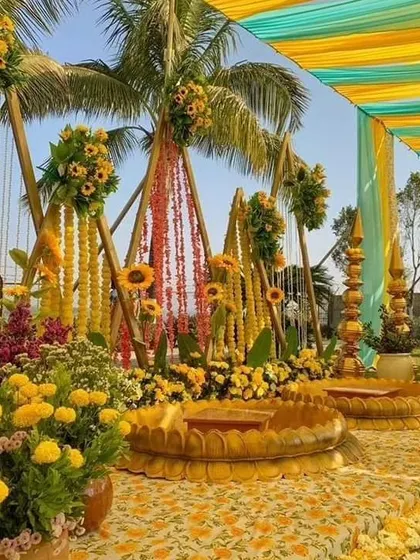 A beautiful outdoor Haldi setup with a floral stage and seating. The design incorporates marigolds, sunflowers, and traditional urlis, all under a canopy of colourful drapes.