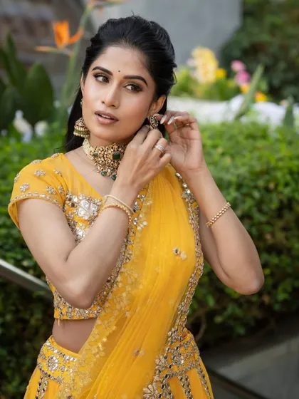 A candid moment of adjusting jewelry, highlighting the detailed eye makeup and radiant skin for a Mehendi ceremony.