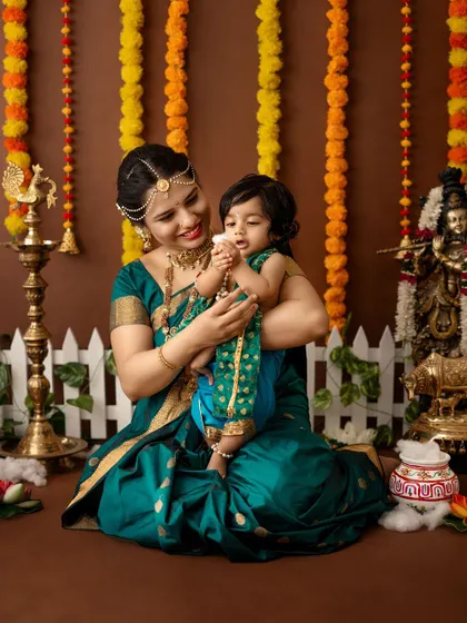 A mother and her baby girl dressed in matching green and blue traditional outfits for a festive shoot.