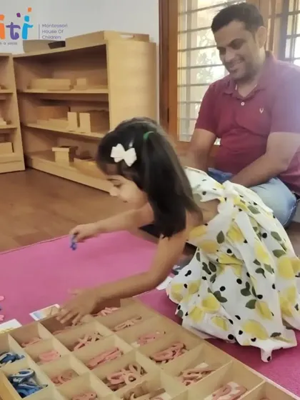 A young girl proudly demonstrates her work with the movable alphabet to her father. This material allows children to begin forming words even before their hands are ready to write.