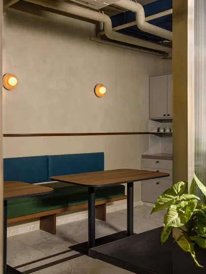 A cozy breakout and pantry area provides a space for informal collaboration and relaxation. We used booth-style seating in shades of blue and green, warm wood tables, and soft lighting to create a comfortable, cafe-like atmosphere within the office.