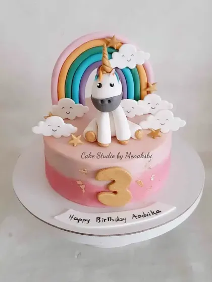 A very cute unicorn themed cake for a 3rd birthday. This design features a sweet unicorn, a pastel rainbow, and smiling clouds in a pink ombre finish.